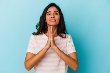 Young caucasian woman isolated on blue background holding hands in pray near mouth, feels confident.