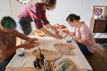 Confident sculptor helping to the girl with special needs making her own plate