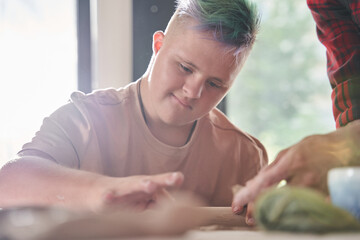 Down syndrome man touching with the finger wet clay while giving shape for it