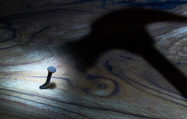 Hammer and nail. The shadow of the hammer hammers a nail into the board. The concept of threat, fear, danger. Light and shadow.