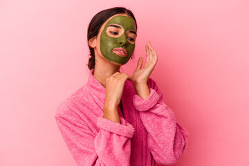 Young caucasian woman wearing a bathrobe and facial mask isolated on pink background