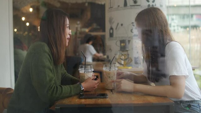 4K Asian woman friends sitting in cafe using smartphone with internet for online message or social media together. Female friendship enjoy outdoor lifestyle with wireless technology and smart gadget