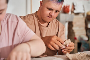 Down syndrome boy with colored hair holding piece of clay and preparing new dish