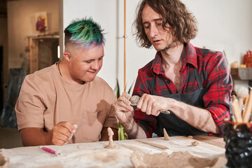 Craftsman showing to his student with down syndrome how to sculpting from the clay