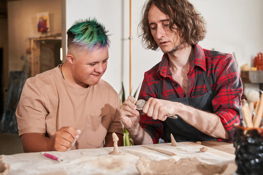 Craftsman showing to his student with down syndrome how to sculpting from the clay