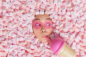 Human face in heart shaped sunglasses drinks fresh cocktail buried in delicious appetizing pink...