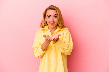 Caucasian blonde woman isolated on pink background holding something with palms, offering to camera.
