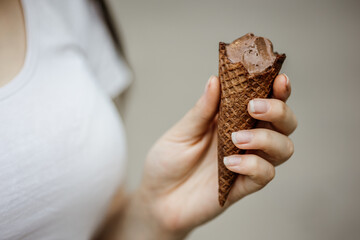 Hand holding ice cream cone. Close up image of woman hand holding fresh waffle cone with chocolate ice cream on the blur background. Walking. Outdoors. Summer and spring vibe in a good mood. Dessert.
