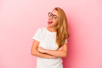 Caucasian blonde woman isolated on pink background funny and friendly sticking out tongue.