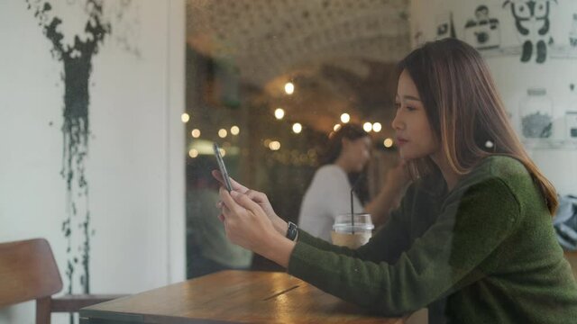 4K Beautiful Asian woman sitting in cafe using smartphone with internet for online shopping or social media. Modern female enjoy outdoor activity lifestyle with wireless technology and smart gadget