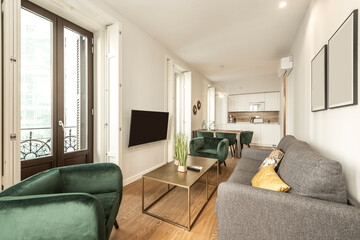 Living room with television in a vacation rental apartment with green velvet sofas, wall air conditioning and large windows