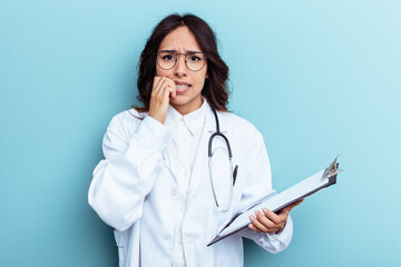 Young doctor mexican woman isolated on blue background biting fingernails, nervous and very anxious.