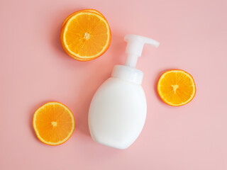 Unbranded pump bottle and orange slices on pink background. Blank container for lotion, cream, sunscreen, shampoo or hair conditioner. Mockup style, cosmetic products advertising, template