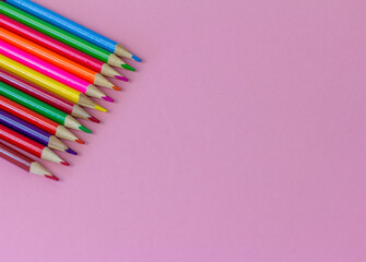 Colored bright pencils on a pink background with a copy of the space.,