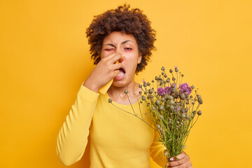 Indoor shot of young Afro American woman suffers from allergic rhinitis uses napkin to blow nose...
