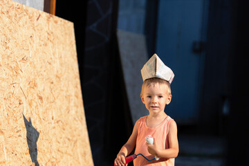 Little blond boy plays builder.Kid in T-shirt, shorts and garrison cap holds a construction...