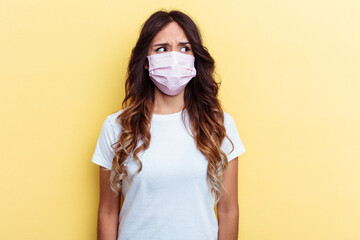 Young mixed race woman wearing a protection for virus isolated on yellow background confused, feels doubtful and unsure.