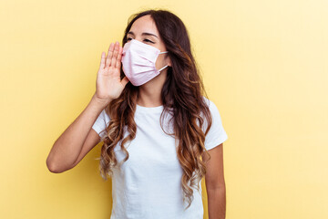Young mixed race woman wearing a protection for virus isolated on yellow background shouting and holding palm near opened mouth.