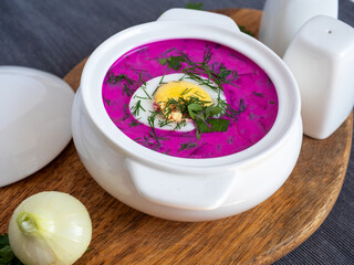Close-up of cold chlodnik soup on a wooden board. Soup of Polish Belarusian and Russian cuisine made of beetroot and kefir, decorated with half an egg. Healthy food