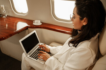 Young woman professional copywriter prints text on her laptop while traveling in an airplane