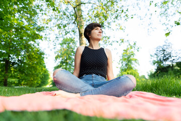 Portrait of an attractive young female sitting with her legs crossed in the park and enjoying summertime in Hyde Park, London