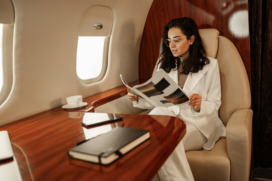 A business class passenger reads a magazine while flying on an airplane