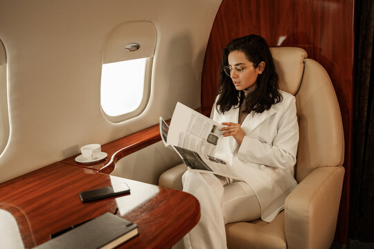 A passenger in a white suit flips through a magazine, reads the news, rests during a flight on a private plane