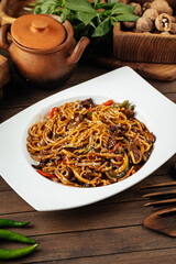 Plate of udon noodles with vegetables and meat on wooden background