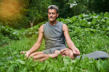 Naklejka na ściany i meble Man practicing yoga and doing ardha padmasana exercise while sitting on lotus position