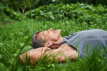 Man laying at the yoga mat at the grass after exercises and relaxing