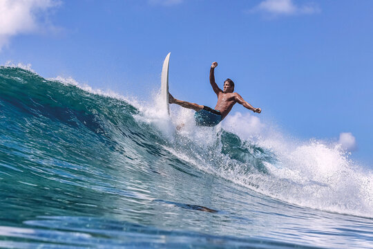 Man with surfboard surfing on sea wave against clear sky