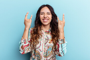 Young mexican woman isolated on blue background showing a horns gesture as a revolution concept.