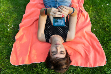 Attractive young female laying down on her towel and using her phone in the park while enjoying summertime in Hyde Park, London