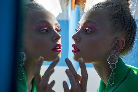 Woman with bright pink makeup looking attentively at the mirror while posing
