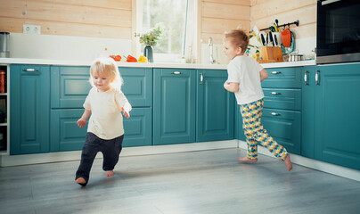 Children's entertainment in the house. Small children run around in the kitchen and play fun games together. Home clothes for the little ones.