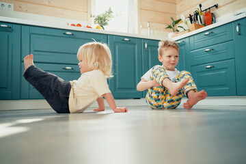 Fototapeta premium Small children run around in the kitchen and play fun games together. Children's entertainment in the house. Home clothes for the little ones.
