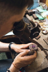 A jeweler uses a microscope to examine the defects of a gold ring with a large purple stone