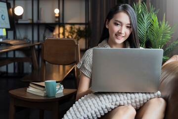 young attrative asian female working at home hand use laptop checking businesss planning report with leisure relax on sofa in living room home isolate concept