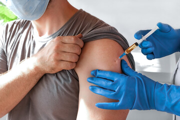 Hands of doctor injecting coronavirus covid-19 vaccine in vaccine syringe to arm muscle of caucasian man for covid immunization.