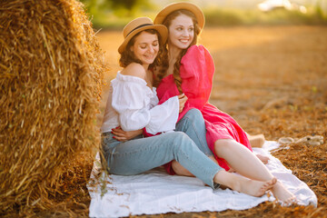 Naklejka na ściany i meble Two young woman in fashionable and stylish clothes posing near hay bales in the countryside. Fashion concept. Nature, vacation, relax and lifestyle.