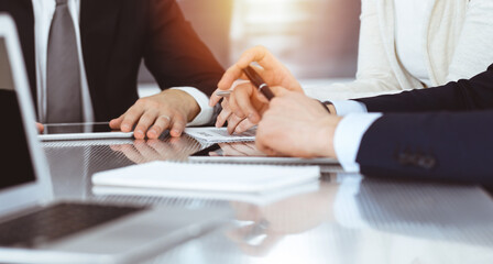 Business people discussing contract while working together in sunny modern office. Unknown businessman and woman with colleagues or lawyers at meeting