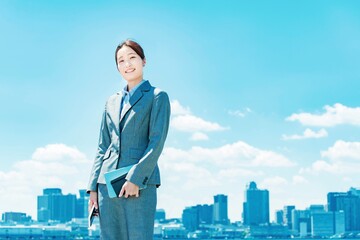 都心と青空を背景に立つ若いビジネスウーマン