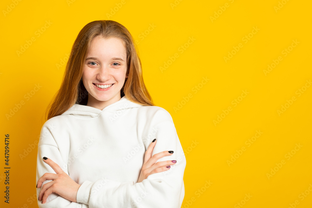 Wall mural Beautiful teenage girl in a white hoodie cute smiling on yellow background. - Wall murals