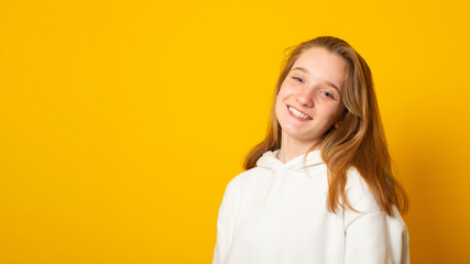Obraz premium Banner copy space. Portrait of a beautiful teenage girl in a white hoodie cute smiling on yellow background.