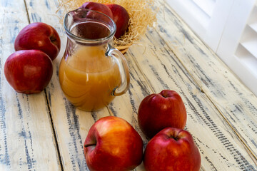Red apples in a basket and apple juice in a jug on a wooden table