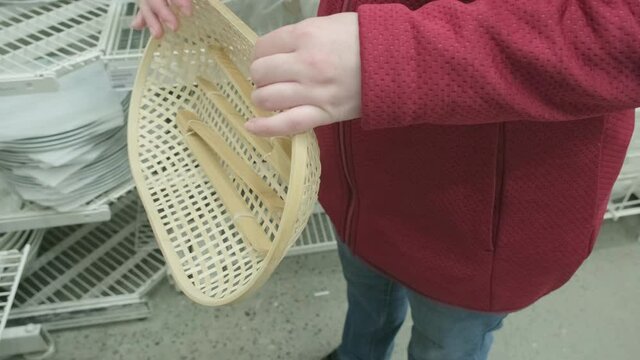 Caucasian girl buys wooden, wicker bread dishes with wooden tongs in a store. The concept of buying new dishes and kitchen equipment. Hands close up shot