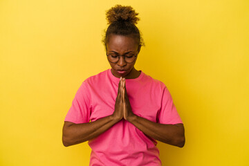 Young african american woman isolated on yellow background praying, showing devotion, religious person looking for divine inspiration.