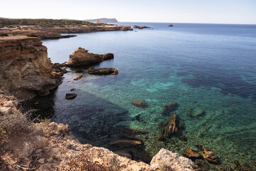 Cala roja in Ibiza, rocky seashore with crystal blue water, Spain