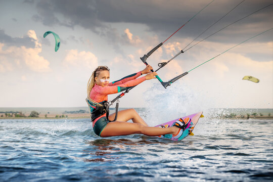 Front view Professional kite surfer woman rides on a board with a plank in her hands on a leman lake with sea water at evening. Water splashes and sun glare. Water sports