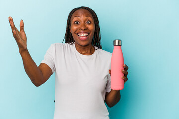 Young african american woman holding canteen isolated on blue background receiving a pleasant surprise, excited and raising hands.